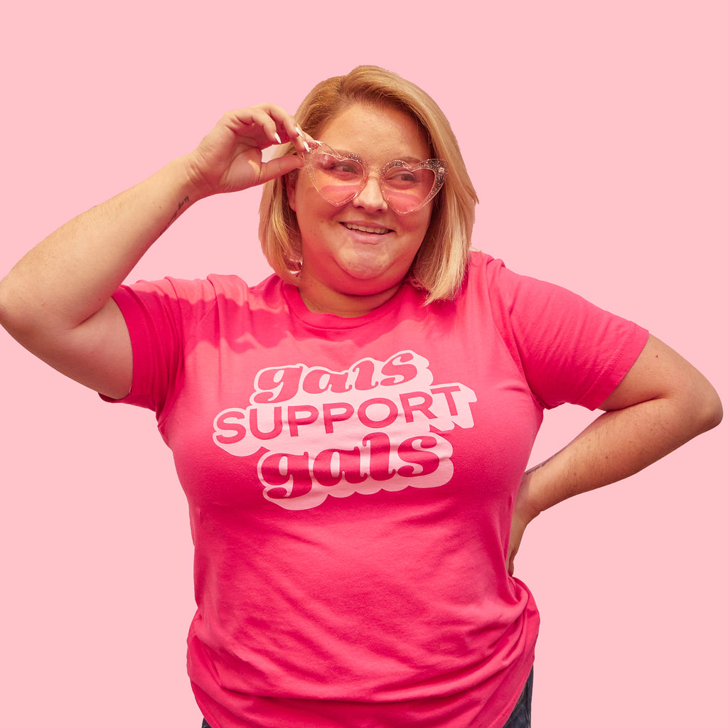 Woman wearing a hot pink graphic t-shirt that says "gals support gals" in bubbly light pink text. Shirt designed by Woman-Owned Wallet, a feminist gift shop located in Louisville KY.