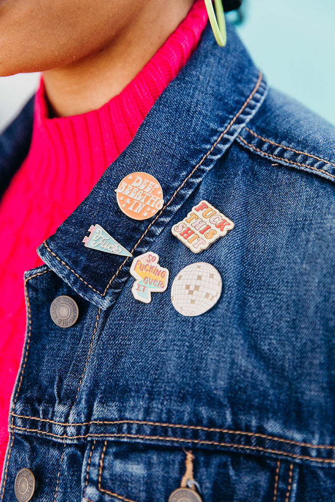 Close up of 5 enamel pins on the lapel of a woman's jean jacket. Each enamel pin features a bold feminist phrase. These pins are sold at Woman-Owned Wallet, a feminist gift shop in Louisville KY.