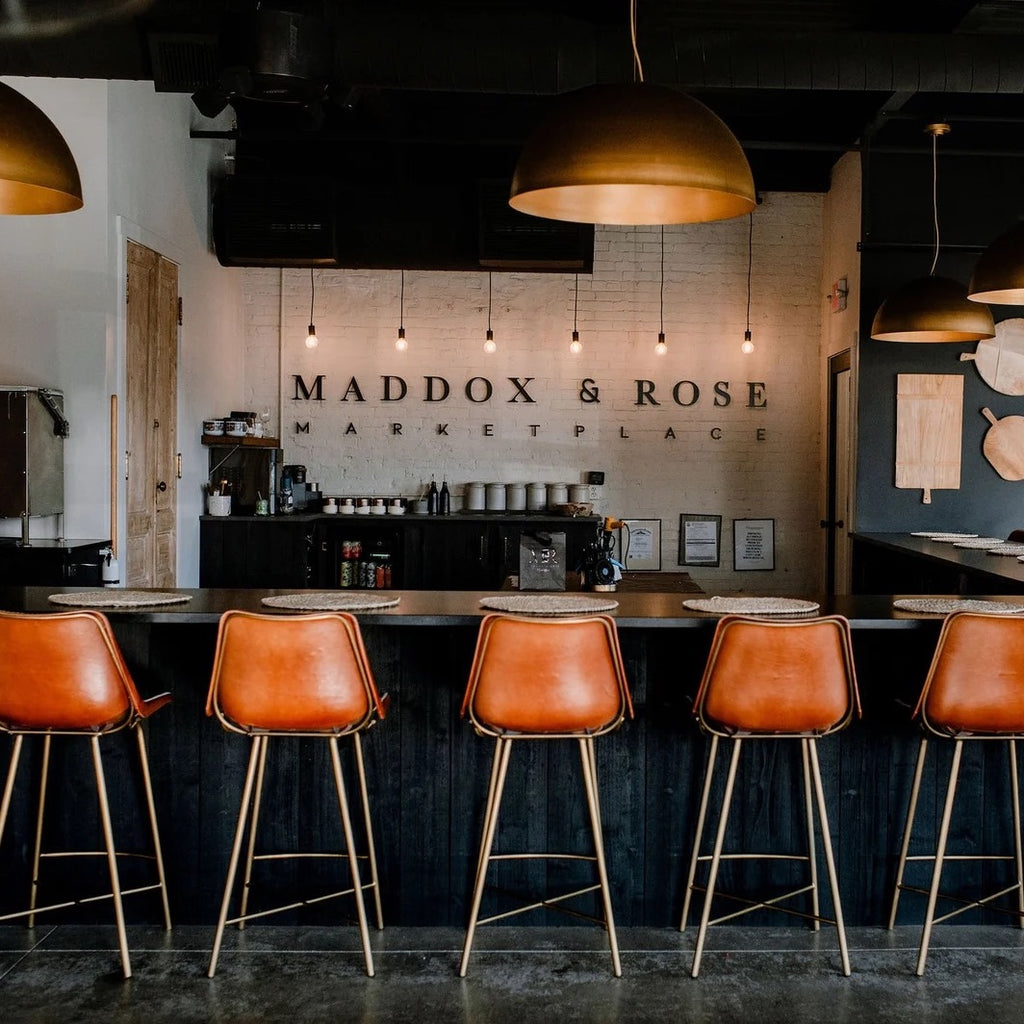 Photo of the Maddox and Rose custom candle bar with 5 tall leather chairs, beautiful hanging lights, and the company's logo. This is one of the featured businesses on the Nulu Woman-Owned Walking Tour and in the Woman-Owned Directory.