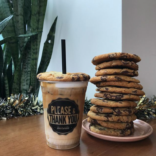 Iced coffee and a tall stack of chocolate chip cookies sitting on a table with green plants in the background. Items are from Please and Thank You, one of the businesses featured on the Nulu Woman-Owned Walking Tour and Woman-Owned Directory hosted by WOW