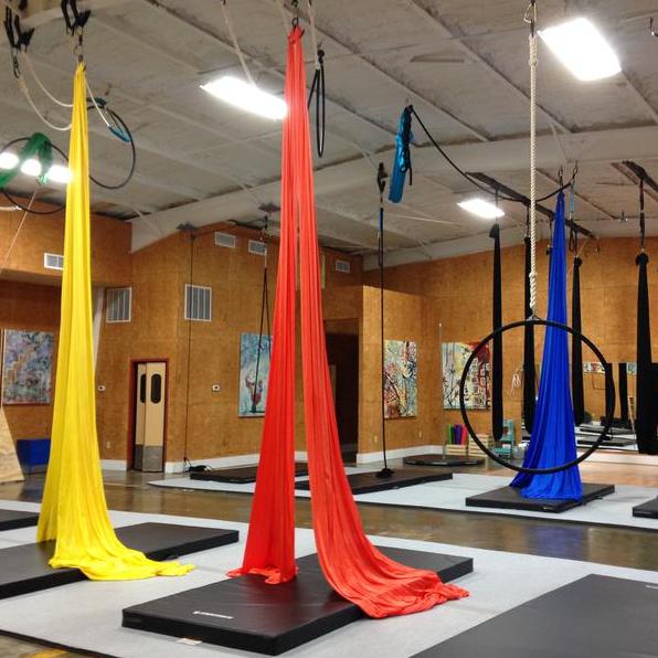 Fitness gym with multiple stations consisting of black floor mats and aerial silks of different colors hanging from the ceiling. This photo is of the gym space inside Suspend Louisville, one of the businesses on the Nulu Woman-Owned Walking Tour.