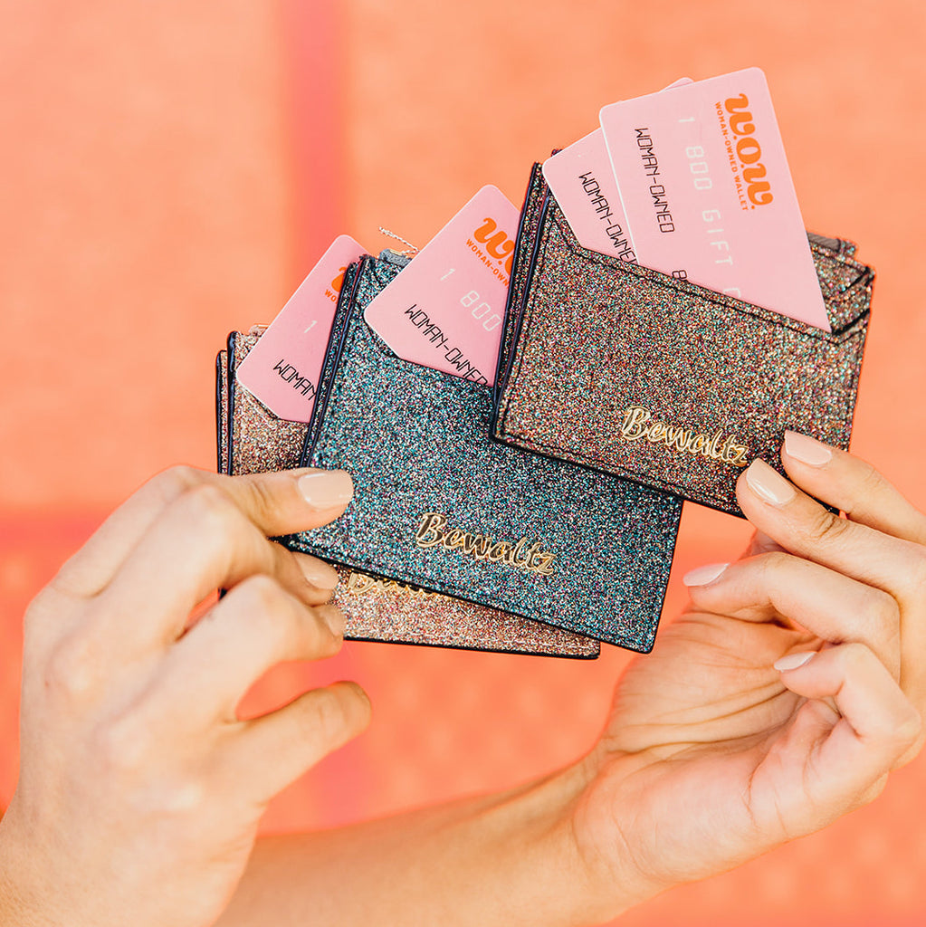 Close up of woman's hands holding glittery wallets containing pink gift cards for Woman-Owned Wallet, a feminist gift shop in Louisville KY.