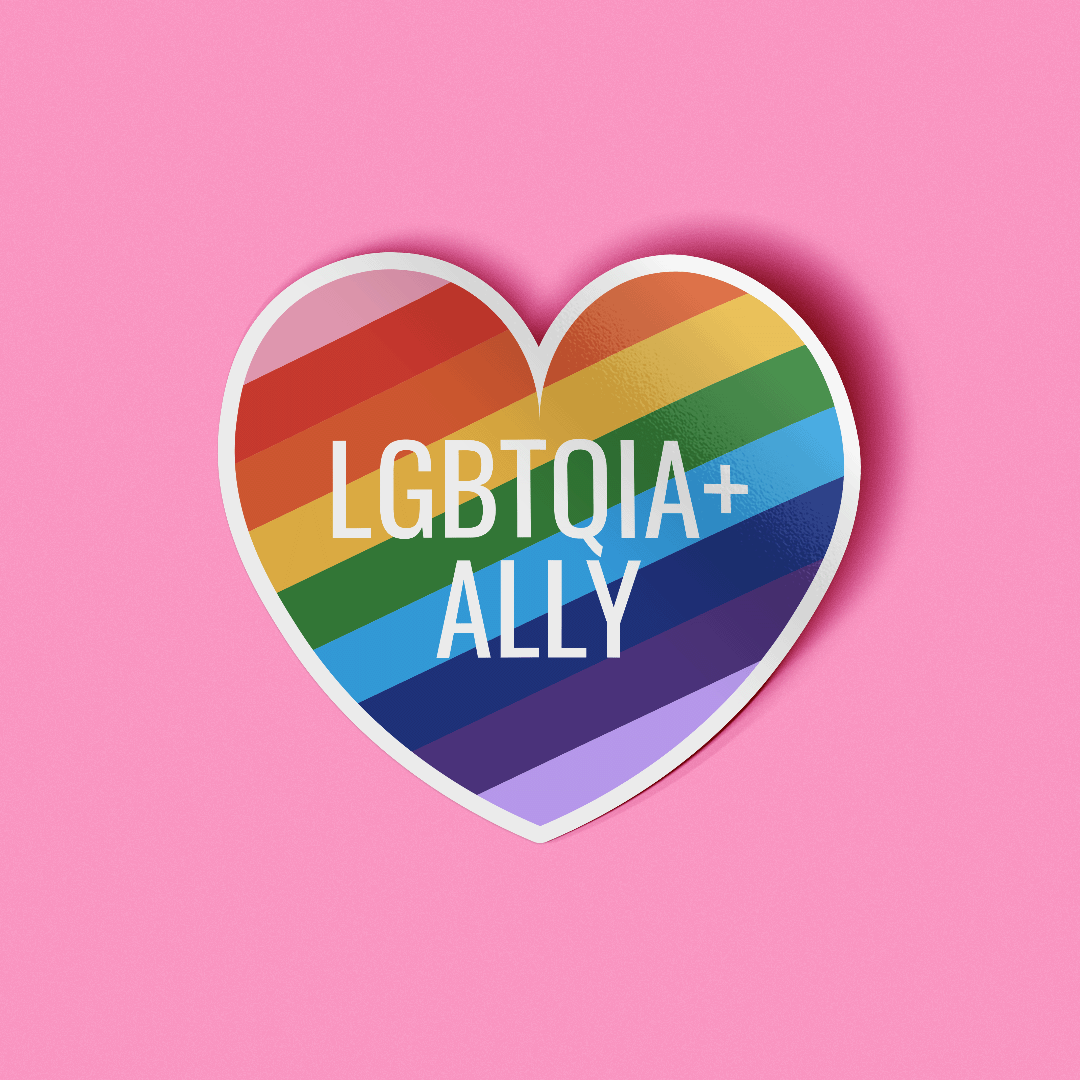 Heart shaped sticker that features the words "LGBTQIA+ Ally" in white text on top of a rainbow striped background.