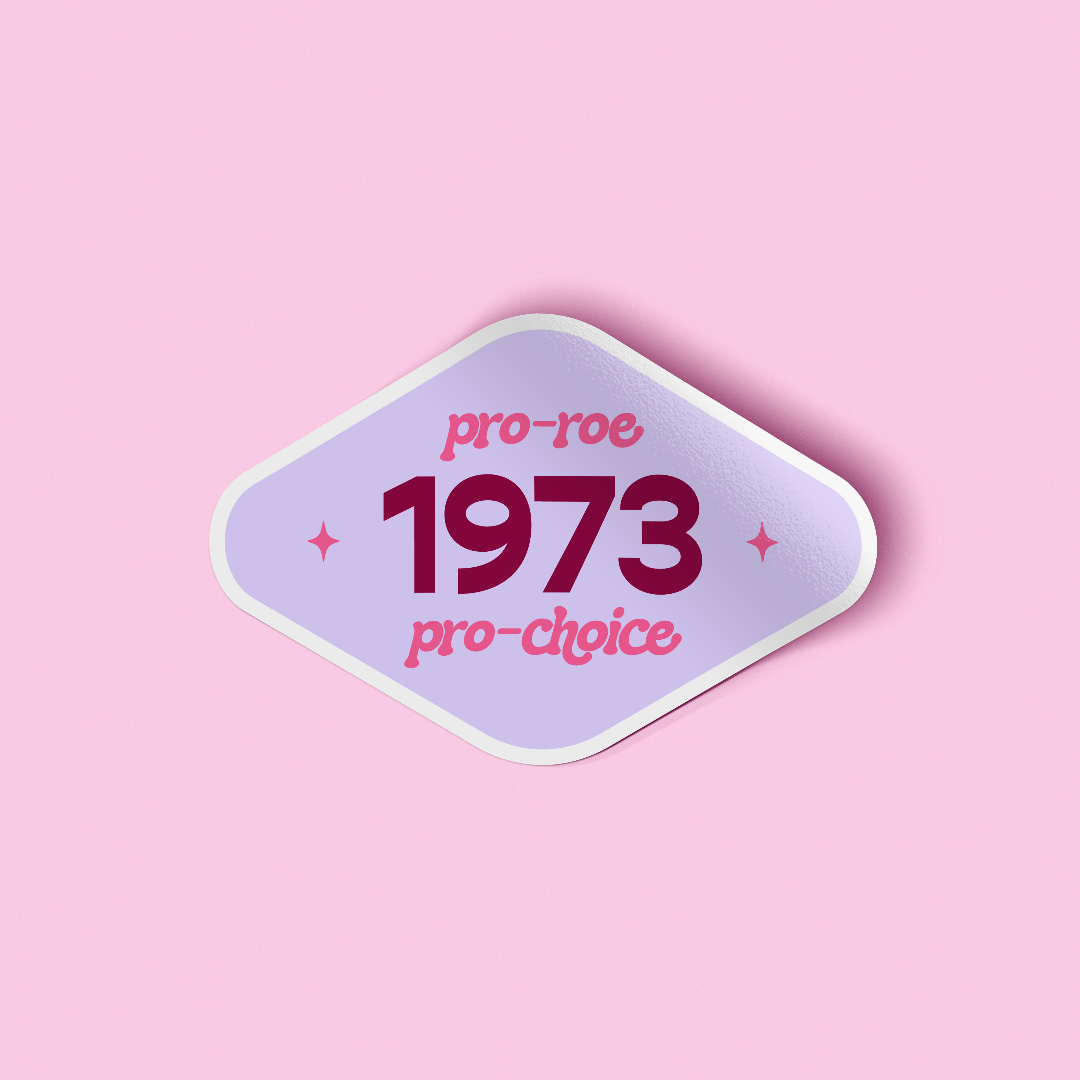 Diamond shaped decorative sticker that says "Pro-Roe Pro-Choice 1973" in funky 70s style fonts. The background of the sticker is light purple and the text is hot pink and maroon. The sticker is laying on a light pink background.