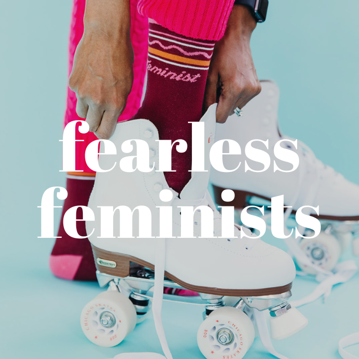 Close up of woman putting her foot into a white roller skate. She is wearing maroon and hot pink sock that say "feminist" on them. The words "Fearless Feminists" are displayed in the center of the photo.