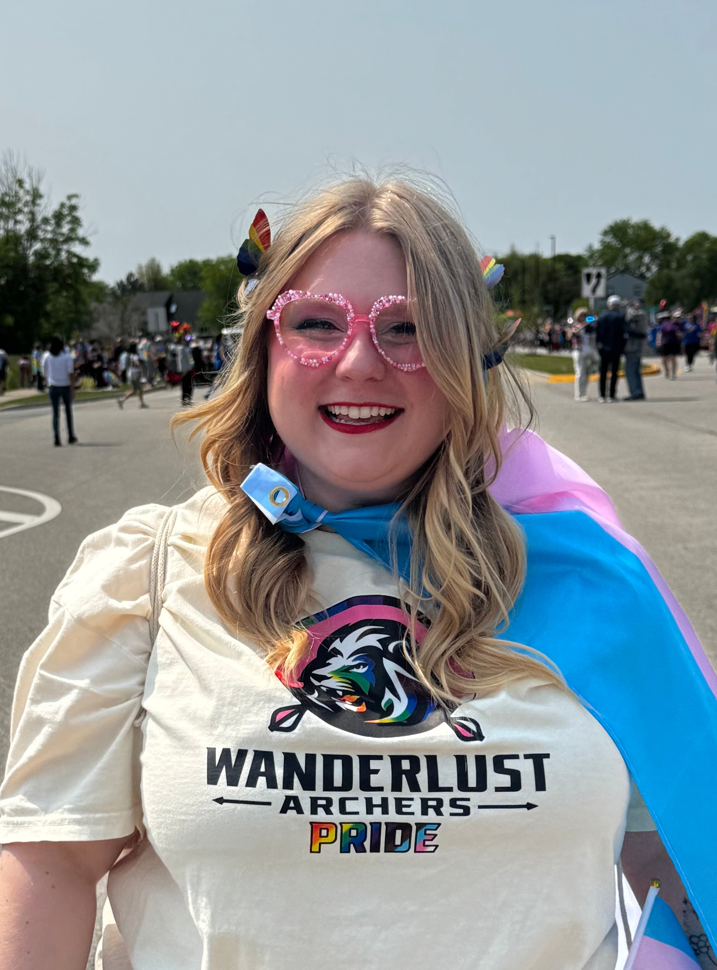 Person wearing a 'Wanderlust Archers Pride' shirt with colorful accessories on a street.