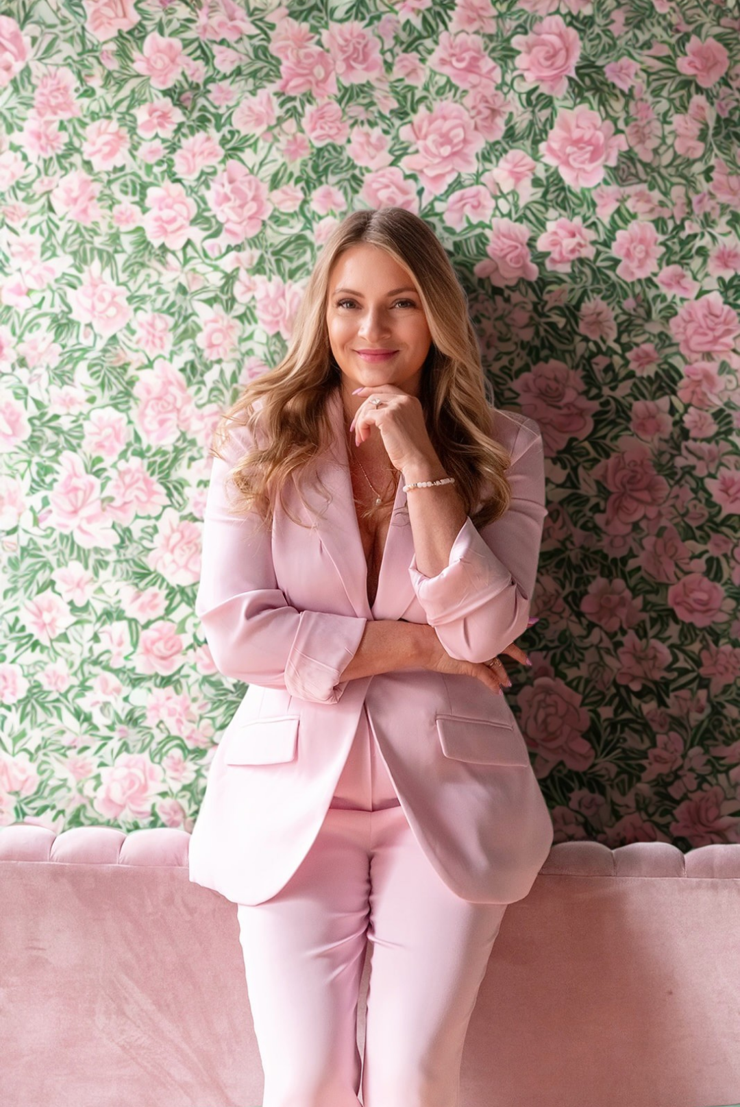 Woman in a pink suit standing against a floral wallpaper background