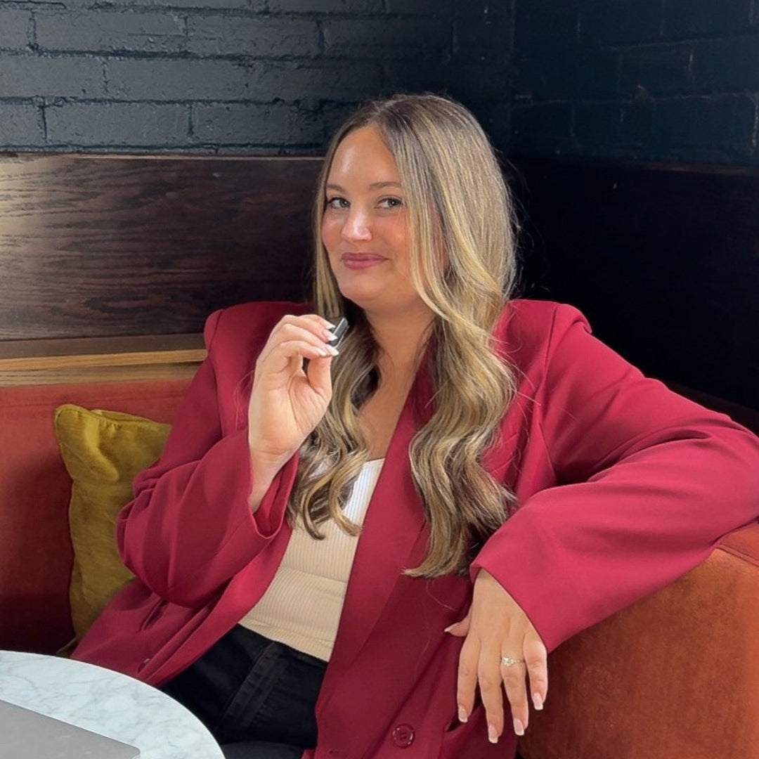 Woman in a red blazer sitting on a couch with a dark brick wall background