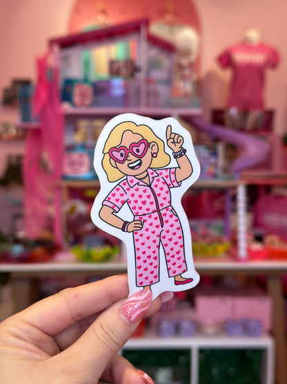 Hand holding a sticker of a character in pink pajamas against a blurred toy store background.