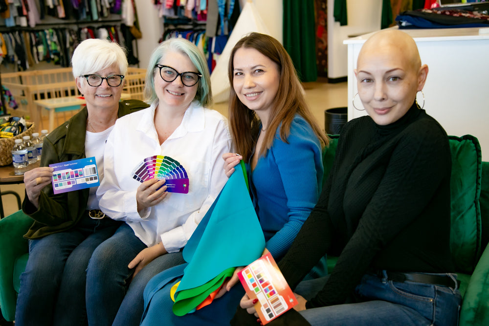 Four women sitting together, holding color swatches in a casual setting.