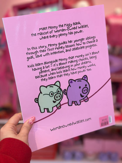 Pink book cover with cartoon pigs and text about Penny the Piggy Bank, held by a person.