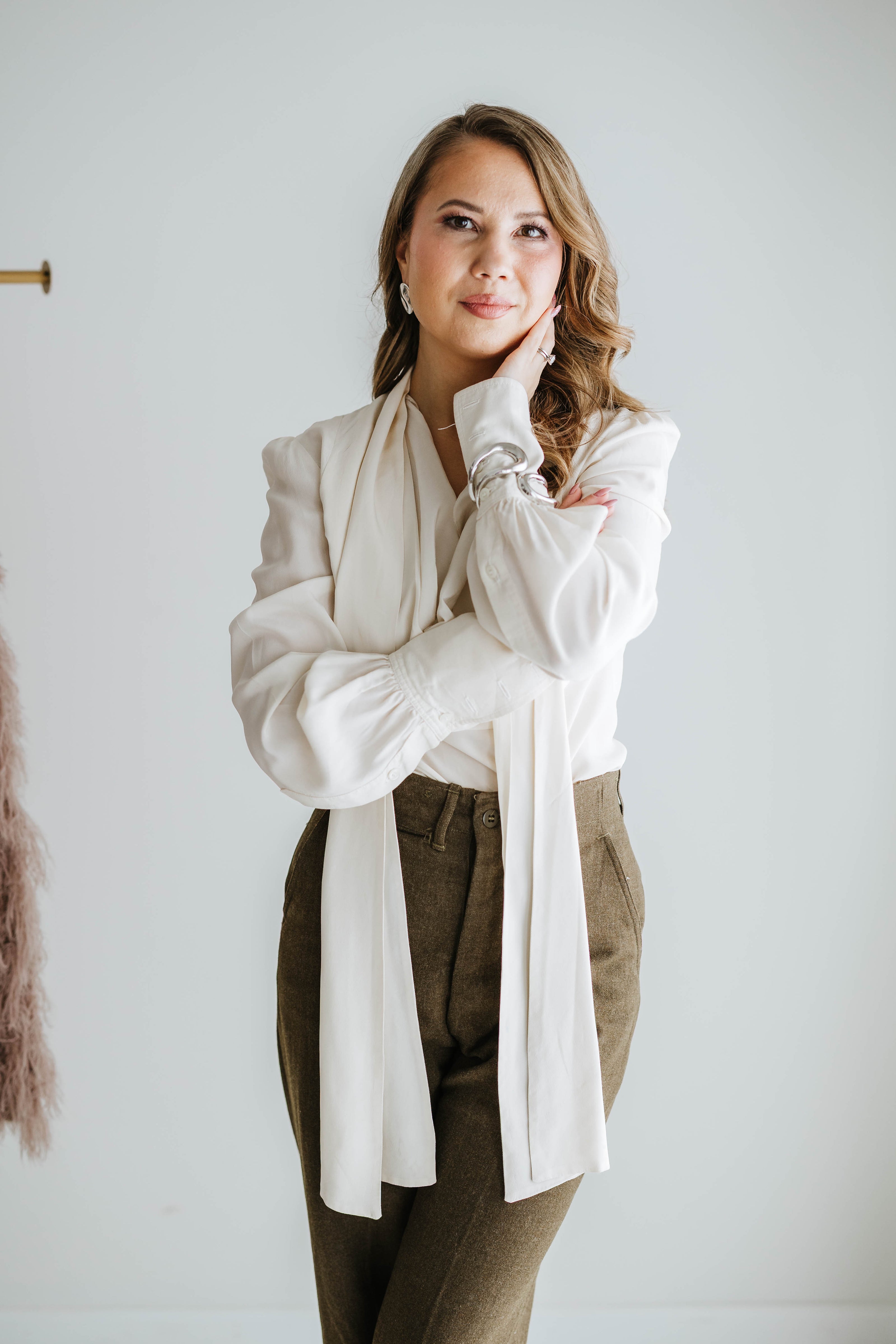 Woman wearing a white blouse and beige pants against a plain background