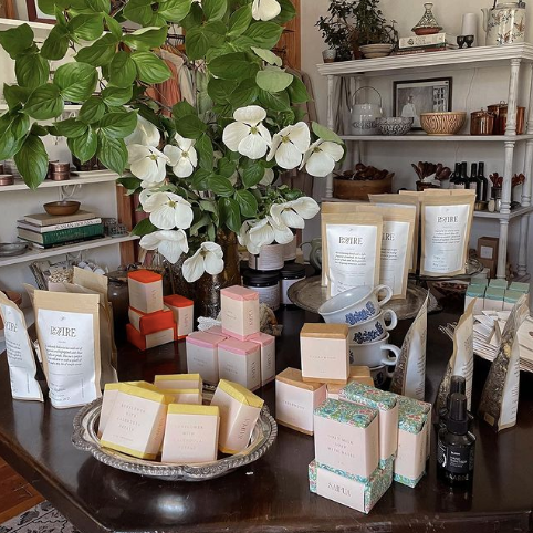 Dark wooden table filled with luxury wellness products including soaps, bath soaks, etc. from shopPAIRE, one of the woman-owned businesses featured in the Woman-Owned Directory.