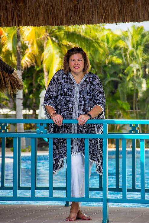 Woman standing by a poolside with palm trees in the background