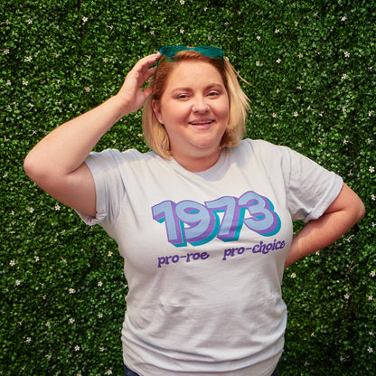 Woman wearing light blue t-shirt that says &quot;1973 Pro Roe, Pro Choice&quot; in light blue, purple, and teal retro-style fonts. Shirt was designed by Woman-Owned Wallet, a feminist gift shop in Louisville KY.