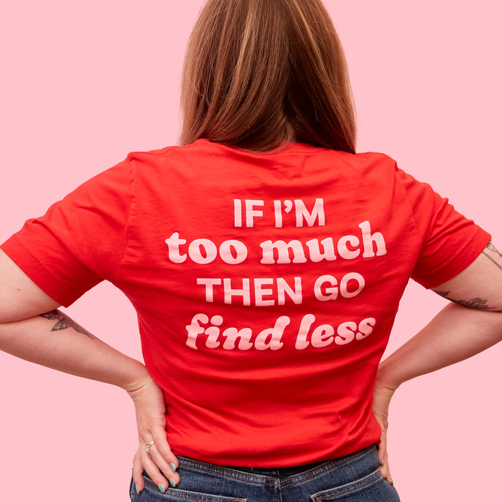 Woman facing away from the camera to show off a red t-shirt that says "If I'm too much, then go find less" in light pink text. T-shirt designed by Woman-Owned Wallet, a feminist gift shop in Louisville KY.