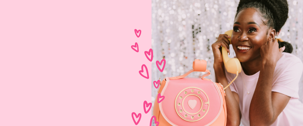 Desktop header graphic split into two sections: on the left is a blank light pink square which allows for text to be placed on top and on the right is a photo of a woman holding a rotary phone up to her ear like she is calling someone. There is a trail of pink hearts in the center.