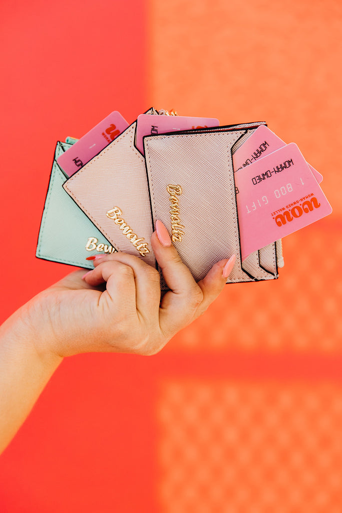 Close up of woman's hand holding three card wallets with pink gift cards inside. The background is a bright pink backdrop. These wallets can be found at Woman-Owned Wallet, a feminist gift shop in Louisville KY.