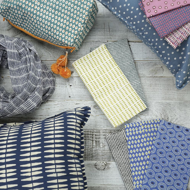 Flatlay photo of textile products such as a scarf, throw pillow, dinner napkins, and makeup bag all in different styles/colors of printed fabric. These products can be found at Graymarket, one of the featured businesses in the Woman-Owned Directory
