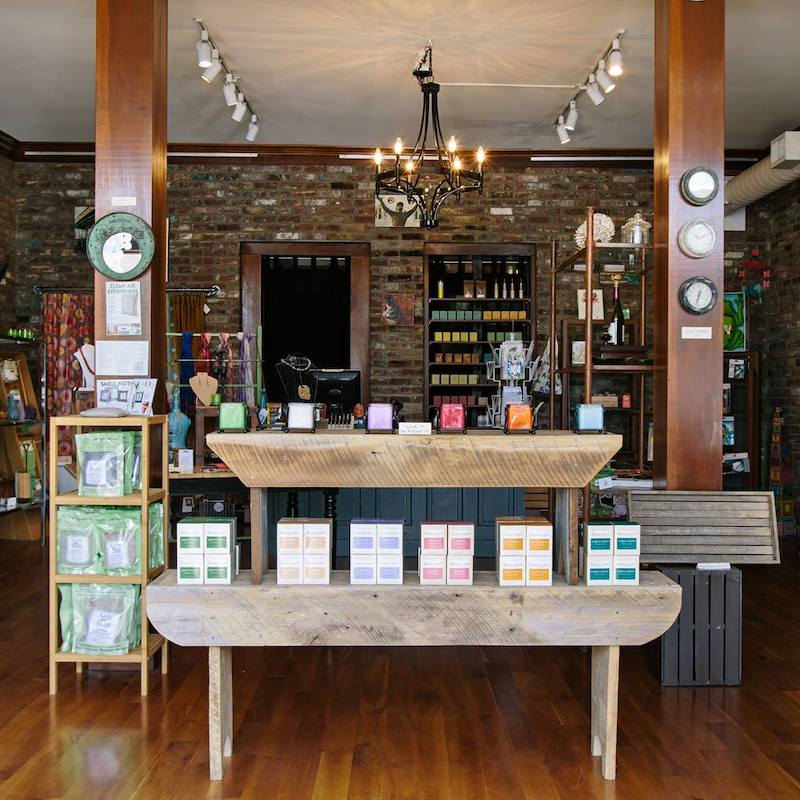 Merchandise table featuring handmade bath products and candles inside the front entrance of Peace of the Earth. This is one of the businesses featured on the Nulu Woman-Owned Walking Tour and in the Woman-Owned Directory.