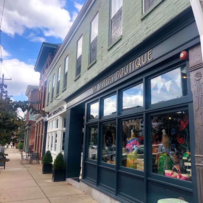Storefront of Six Sisters Boutique is a two story building with green painted brick on the top level and large windows with black trim and the store's logo on the bottom level. This is one of the businesses featured in the Woman-Owned Directory.