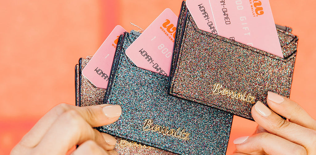 Close up of woman's hands holding glittery wallets containing pink gift cards for Woman-Owned Wallet, a feminist gift shop in Louisville KY.