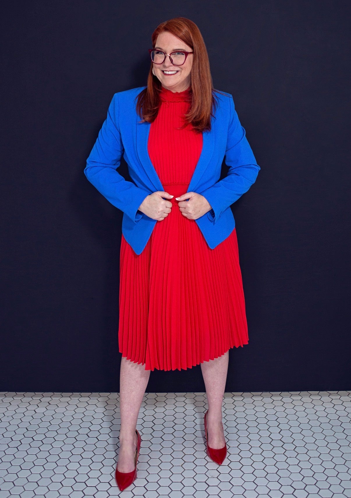 Woman wearing a blue blazer over a red dress against a dark background