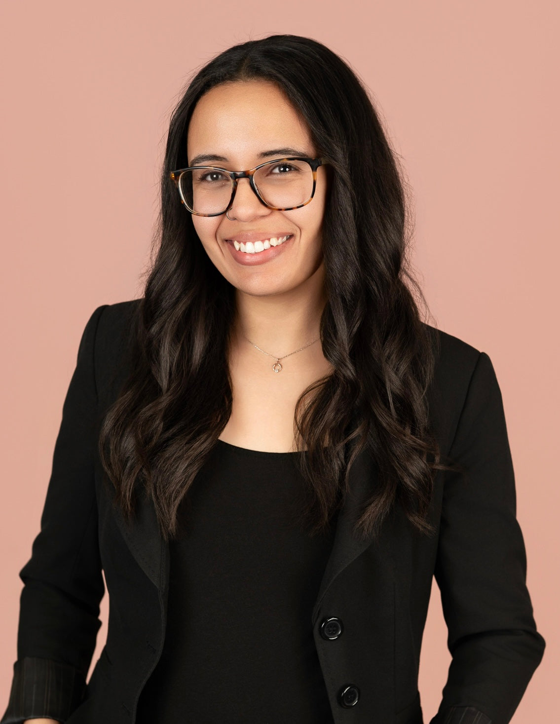 Woman wearing glasses and a black blazer against a pink background