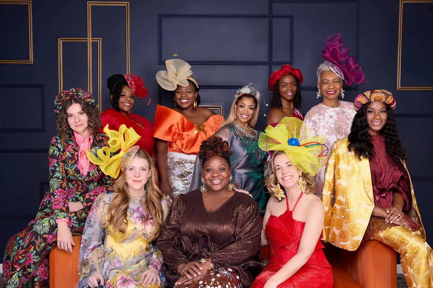 Group of women in colorful outfits with decorative hats against a dark blue wall.