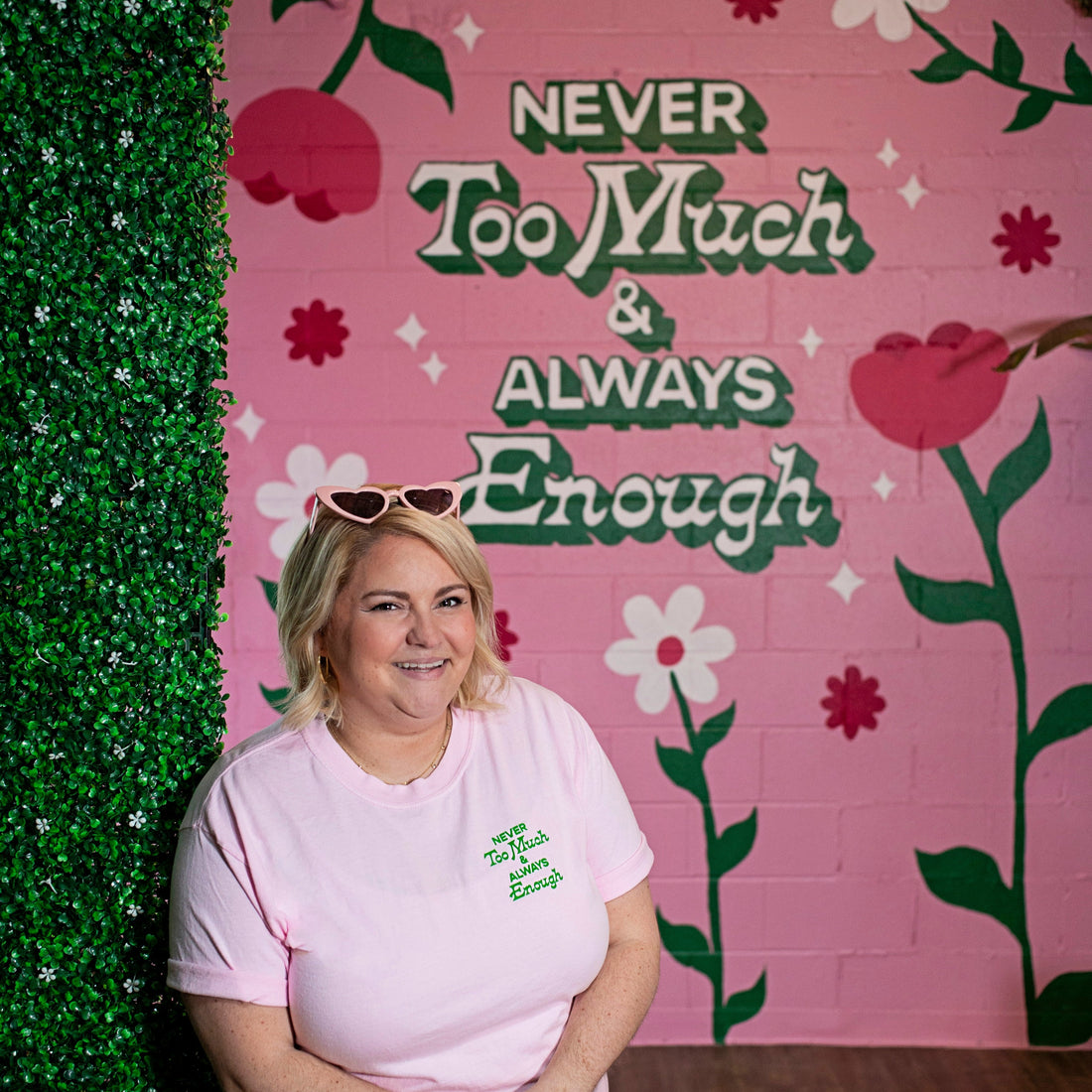 Woman wearing pink tshirt that says &quot;Never Too Much &amp; Always Enough&quot; in small green font near shoulder