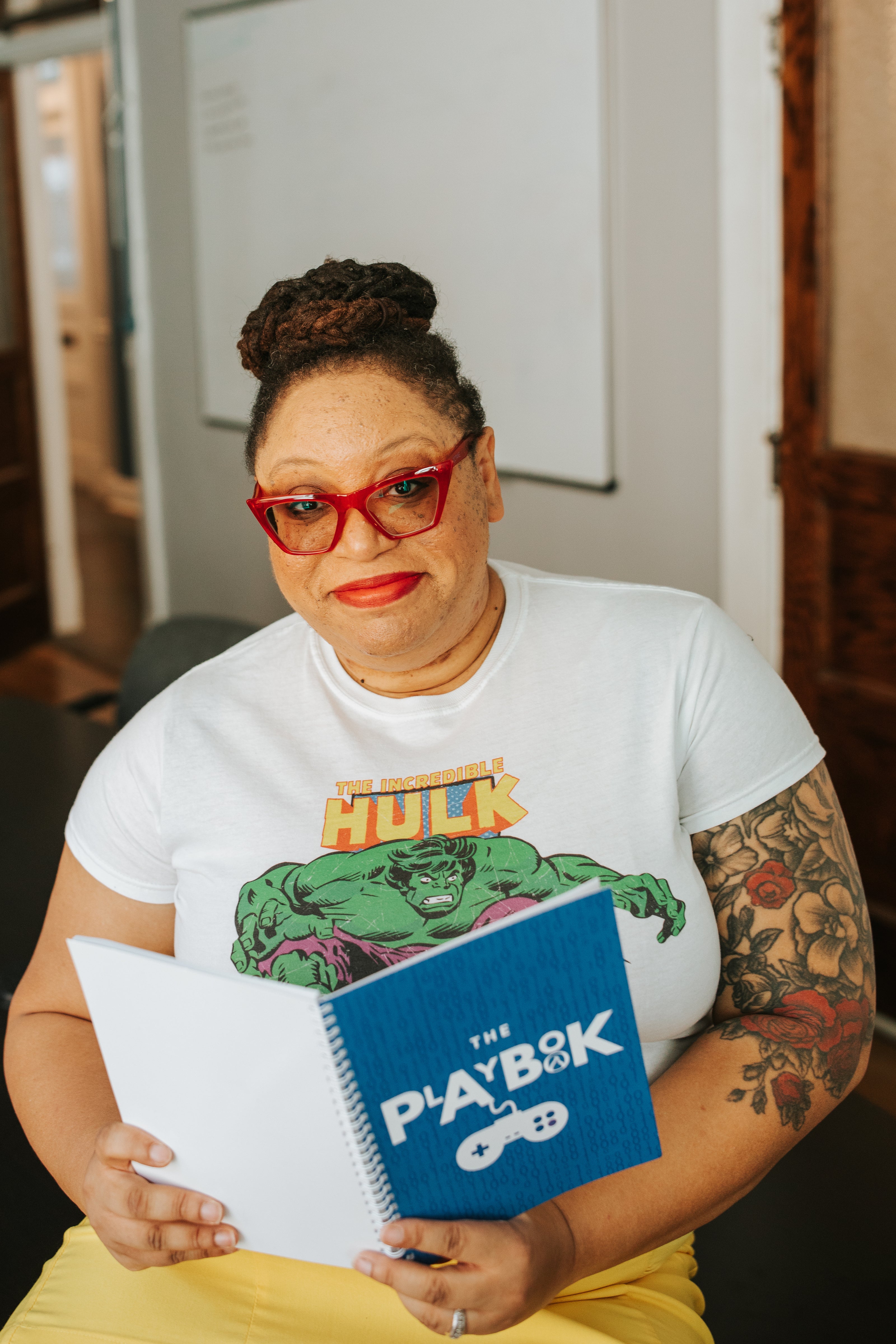 Person wearing a white t-shirt with a superhero design, holding a notebook and a book.