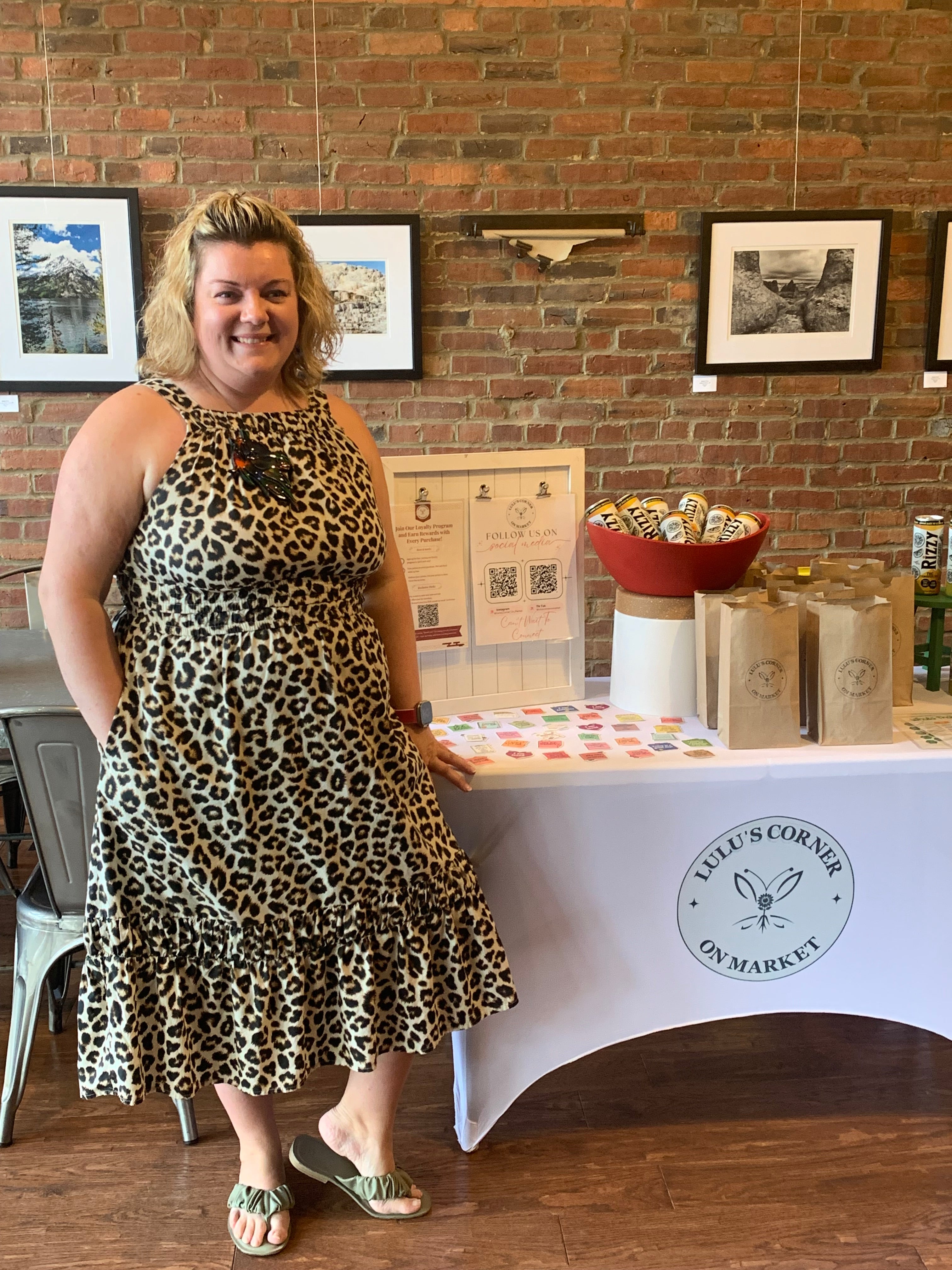 Person wearing a leopard print dress standing in a room with brick walls and framed pictures.