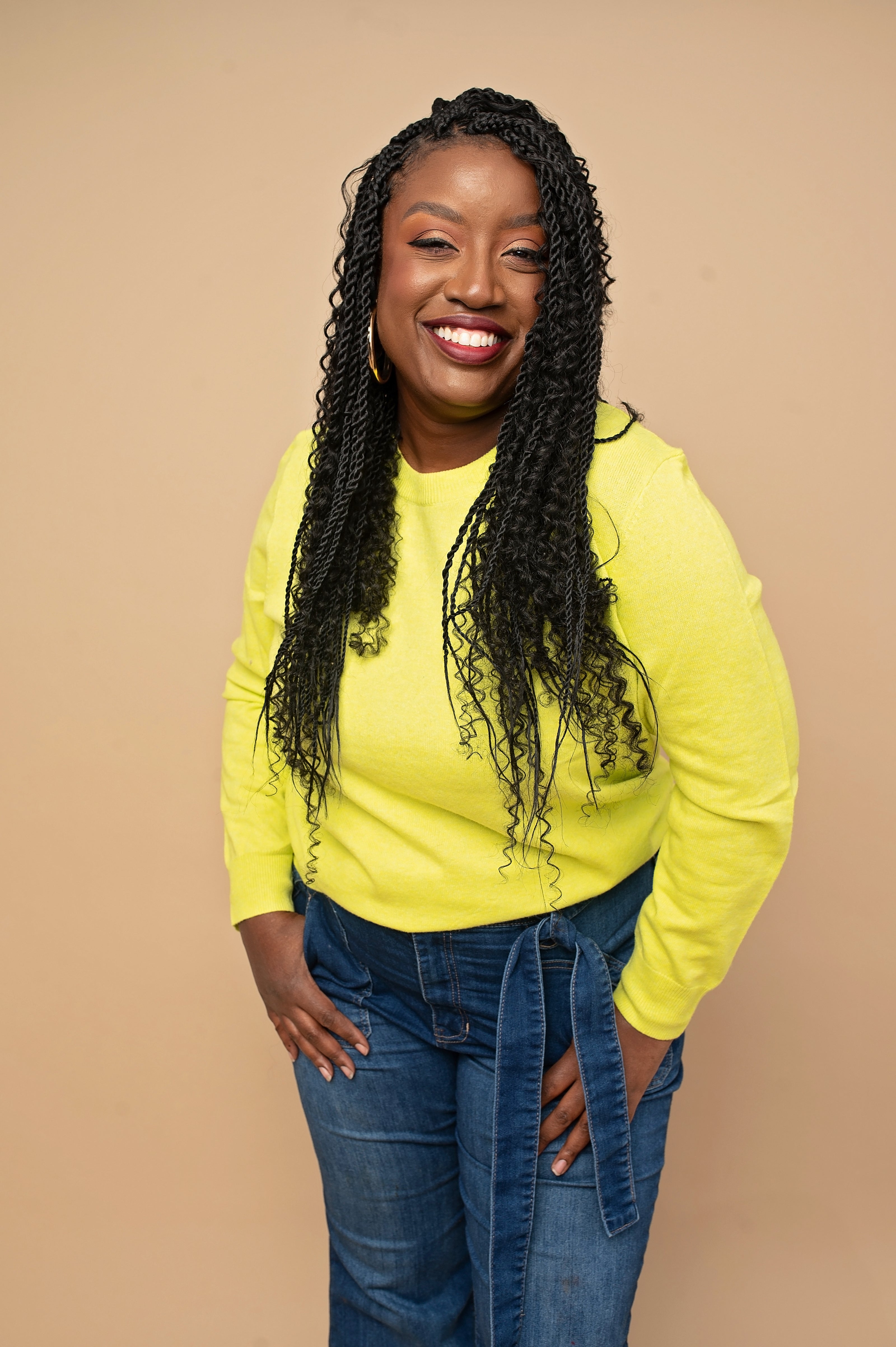 Woman wearing a bright yellow sweater and blue jeans against a beige background
