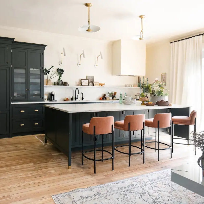 Modern updated kitchen featuring tall dark green cabinetry with large kitchen island and 4 brown leather bar stools. Kitchen is part of stayatPAIRE II, a boutique luxury rental featured in WOW's Woman-Owned Directory.