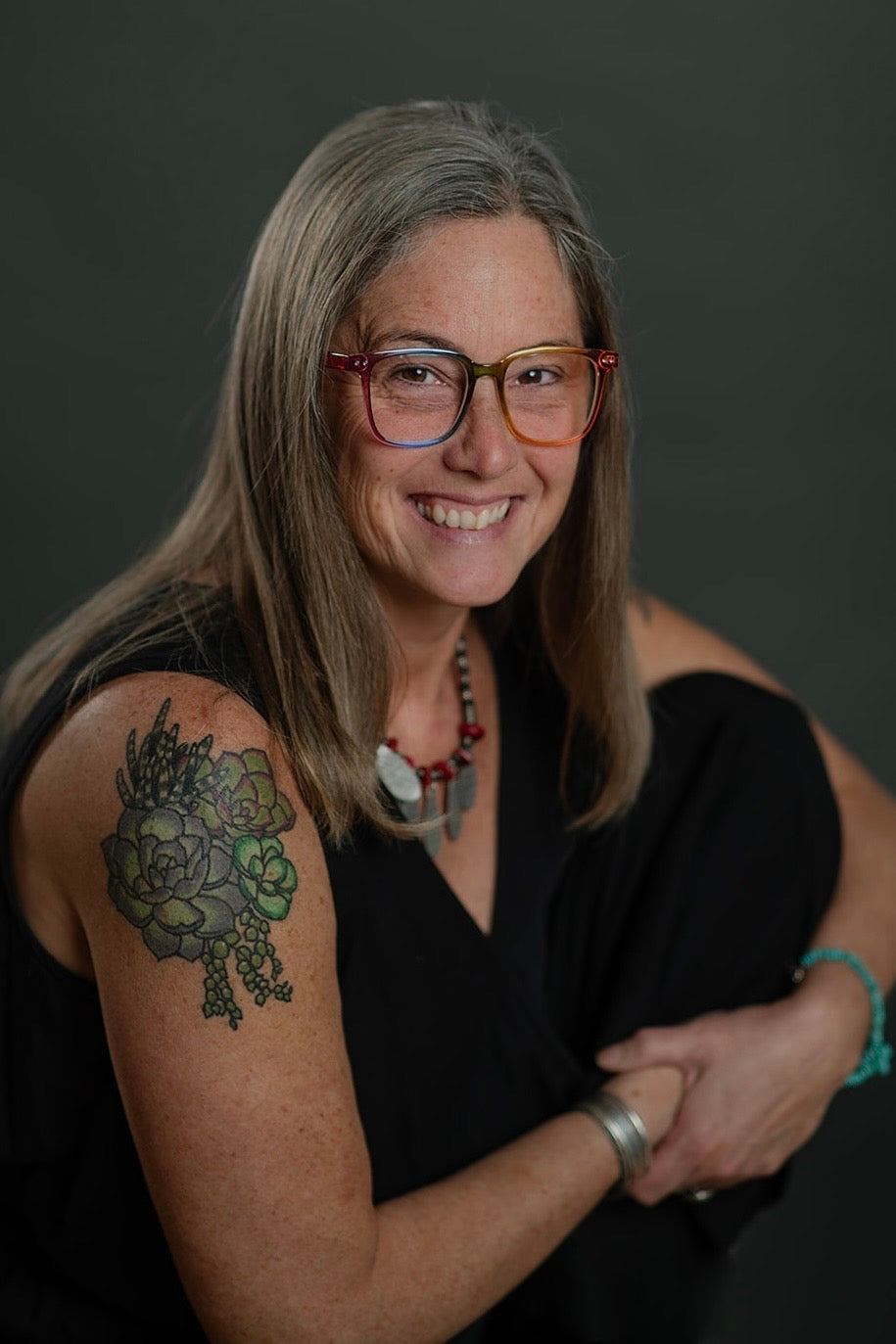 Woman with glasses and a tattoo on her arm against a dark background