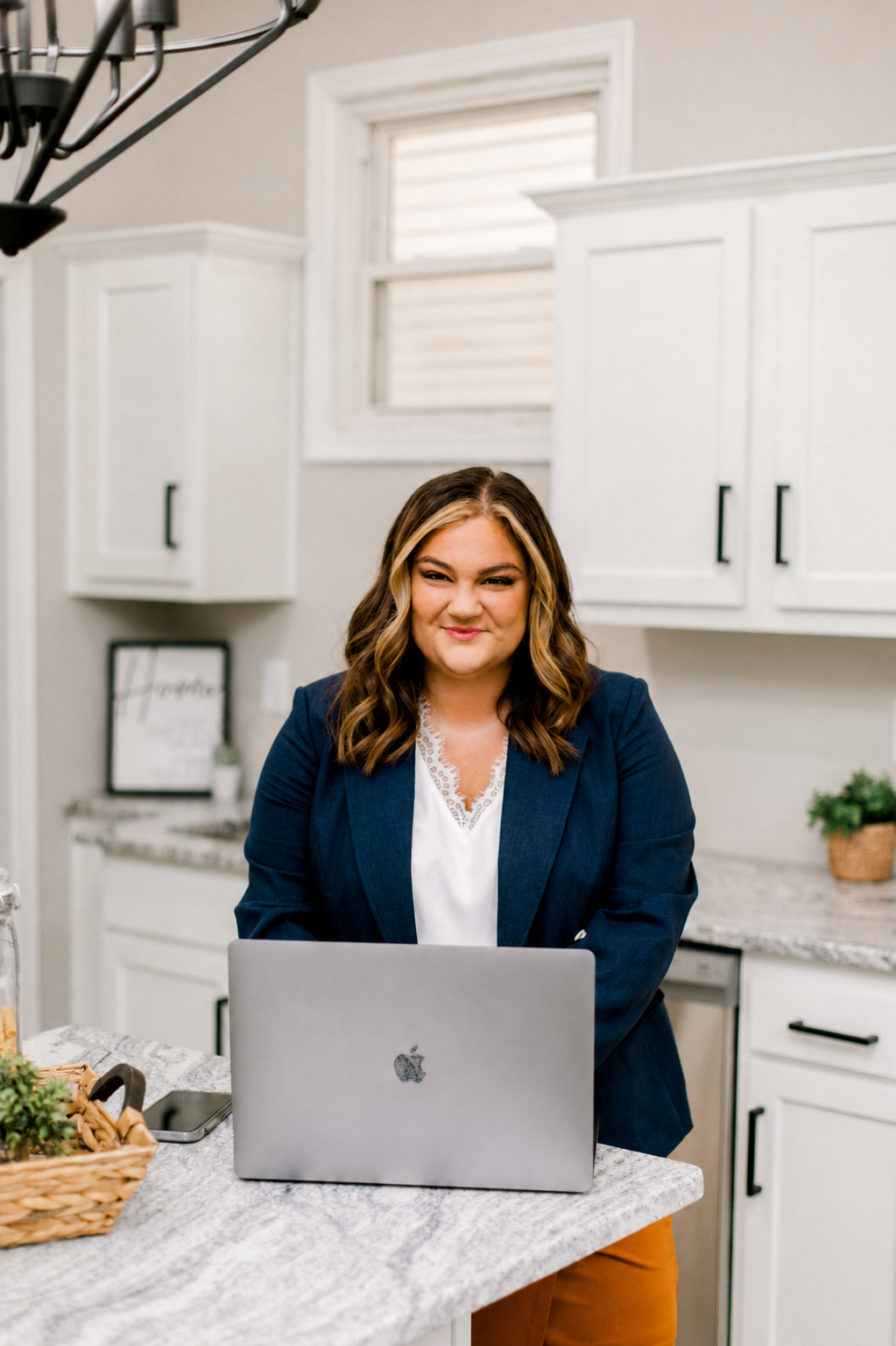 Woman sitting at a kitchen counter with a laptop, wearing a blue blazer.