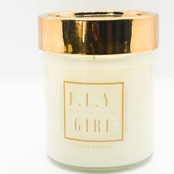 White candle in a clear jar with a gold lid. This candle is from Fly Girl Candles in the scent Citron and Mandarin.