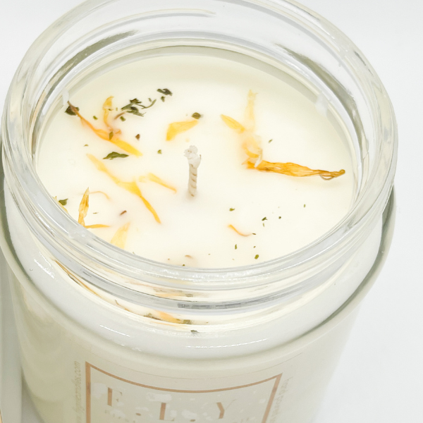 Top view of a white candle in a clear jar featuring dried florals on top. This candle is from Fly Girl Candles in the scent Citron and Mandarin.