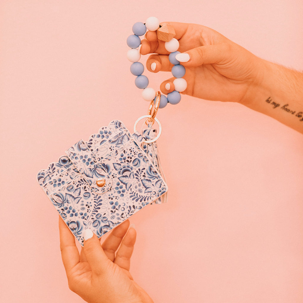 Close up of woman's hands holding a wristlet wallet featuring a blue and white Scandinavian floral pattern.