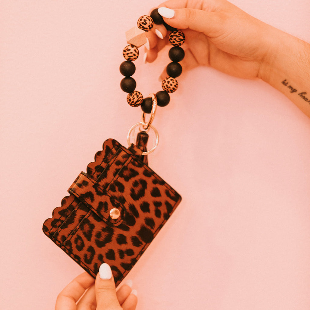 Closeup of woman's hands holding a wristlet wallet featuring a black and brown cheetah print pattern.