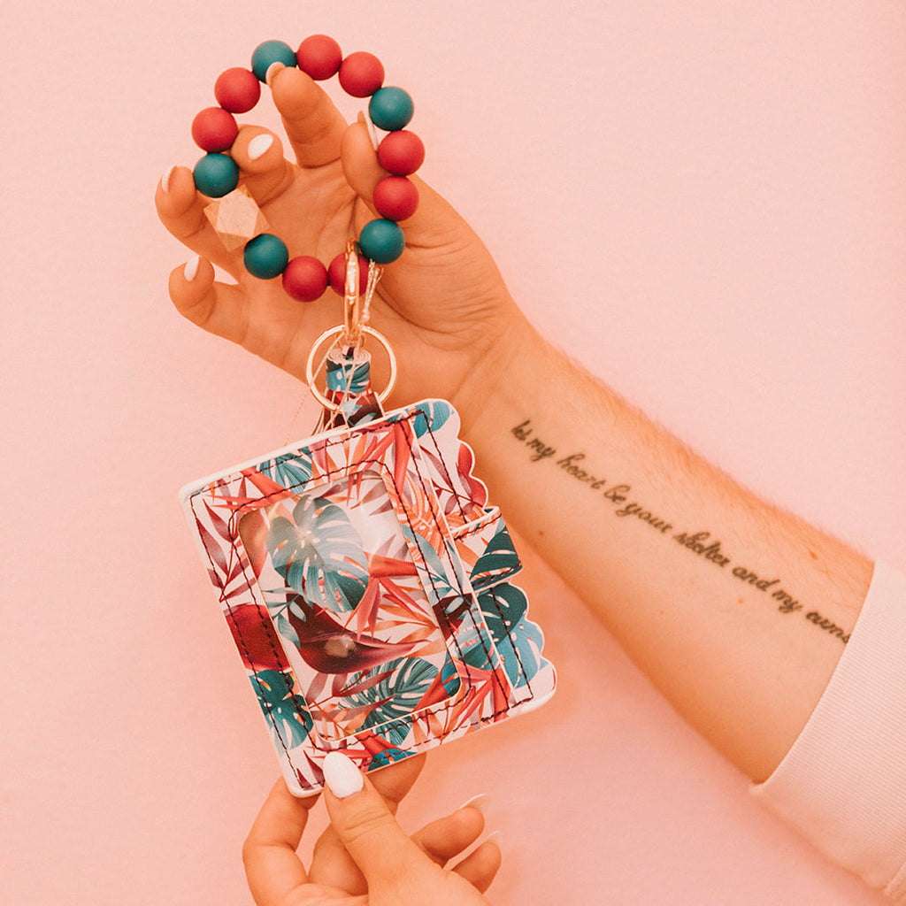 Close up of woman's hands holding a wristlet wallet featuring a deep teal and pink palm tree pattern.