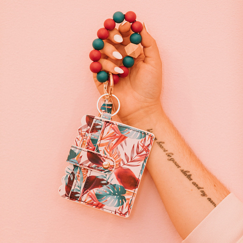 Close up of woman's hands holding a wristlet wallet featuring a deep teal and pink palm tree pattern.