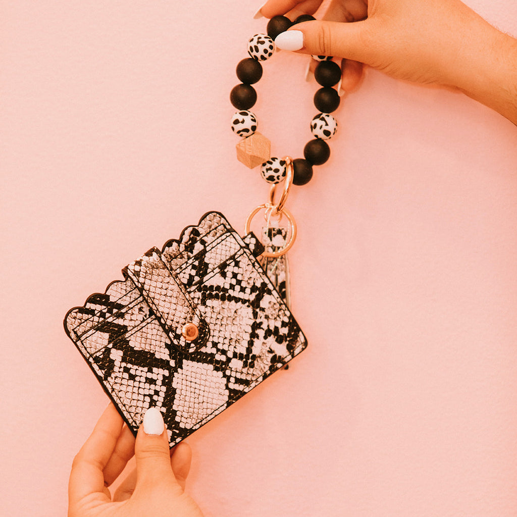 Closeup of woman's hands holding a wristlet wallet featuring a black and white snakeskin pattern.