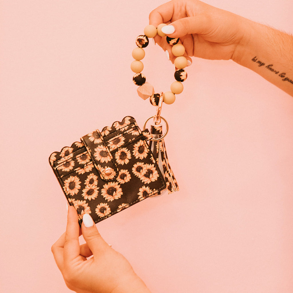 Closeup of woman's hands holding a wristlet wallet featuring a black and yellow sunflower pattern.