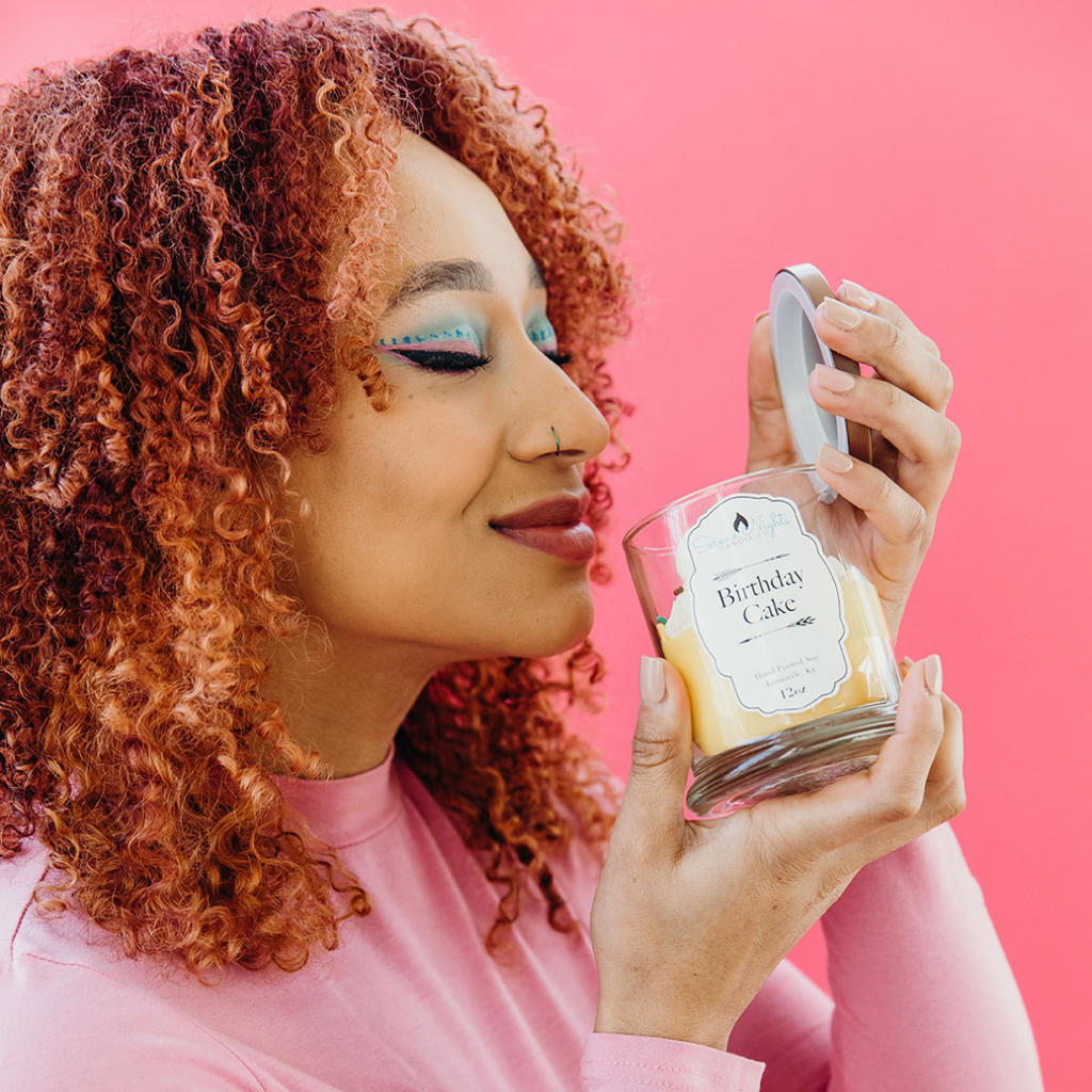 Close up of woman holding and smelling the Birthday Cake candle against pink background