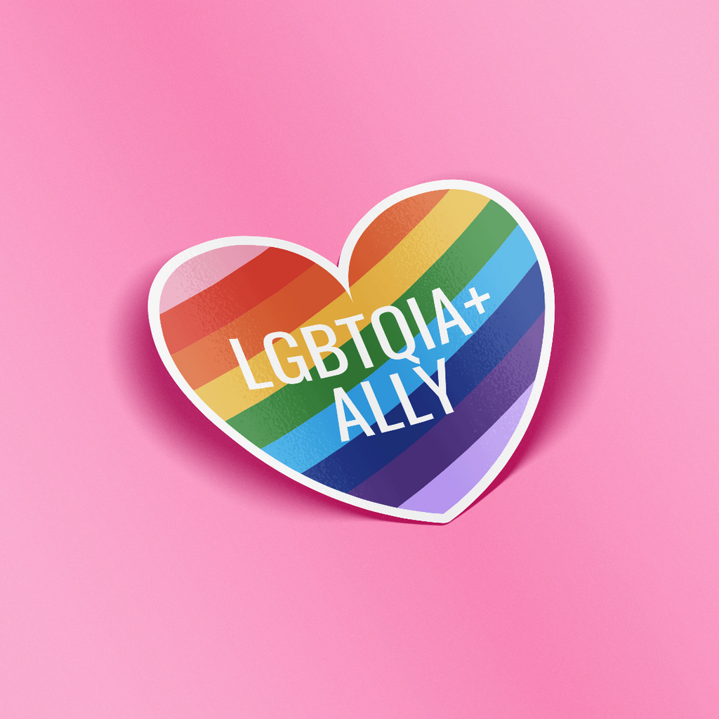 Heart shaped sticker that features the words "LGBTQIA+ Ally" in white text on top of a rainbow striped background. 