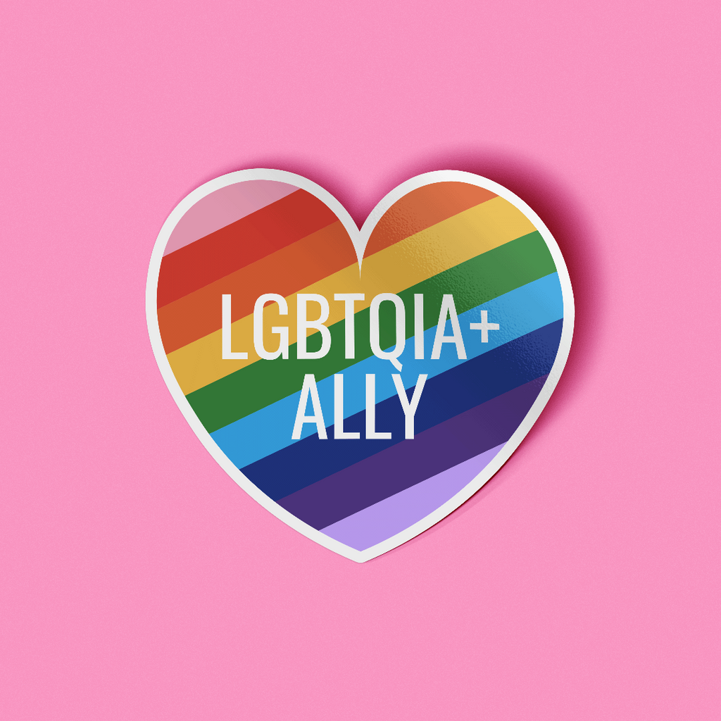 Heart shaped sticker that features the words "LGBTQIA+ Ally" in white text on top of a rainbow striped background. 