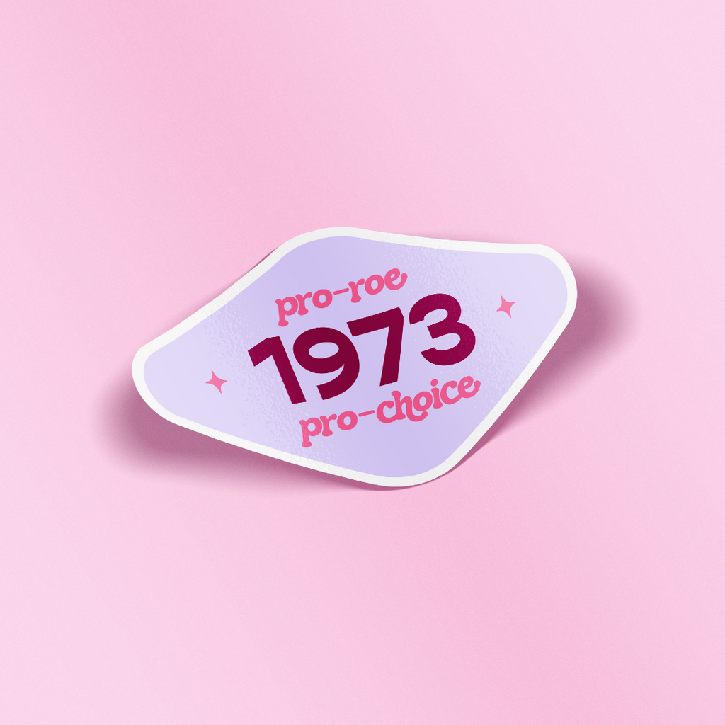 Diamond shaped decorative sticker that says "Pro-Roe Pro-Choice 1973" in funky 70s style fonts. The background of the sticker is light purple and the text is hot pink and maroon. The sticker is laying on a light pink background.