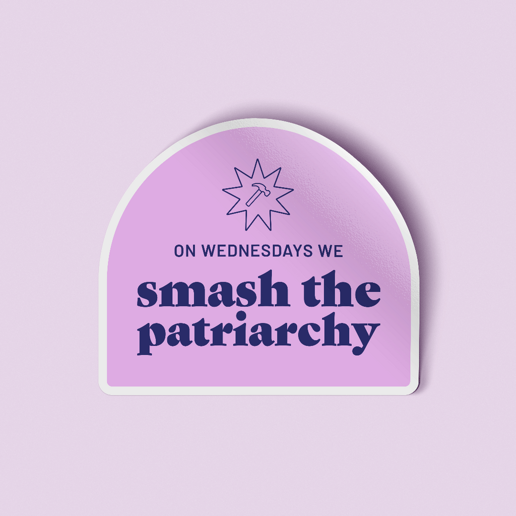 WOW Original decorative sticker that says "On Wednesdays we smash the patriarchy" paired with a hammer symbol all in a deep purple color. The text and illustration is placed on a lilac colored arch. The sticker is laying on a light purple background. 
