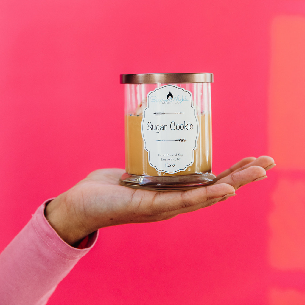 product shot of the sugar cookie candle placed on hand against pink background